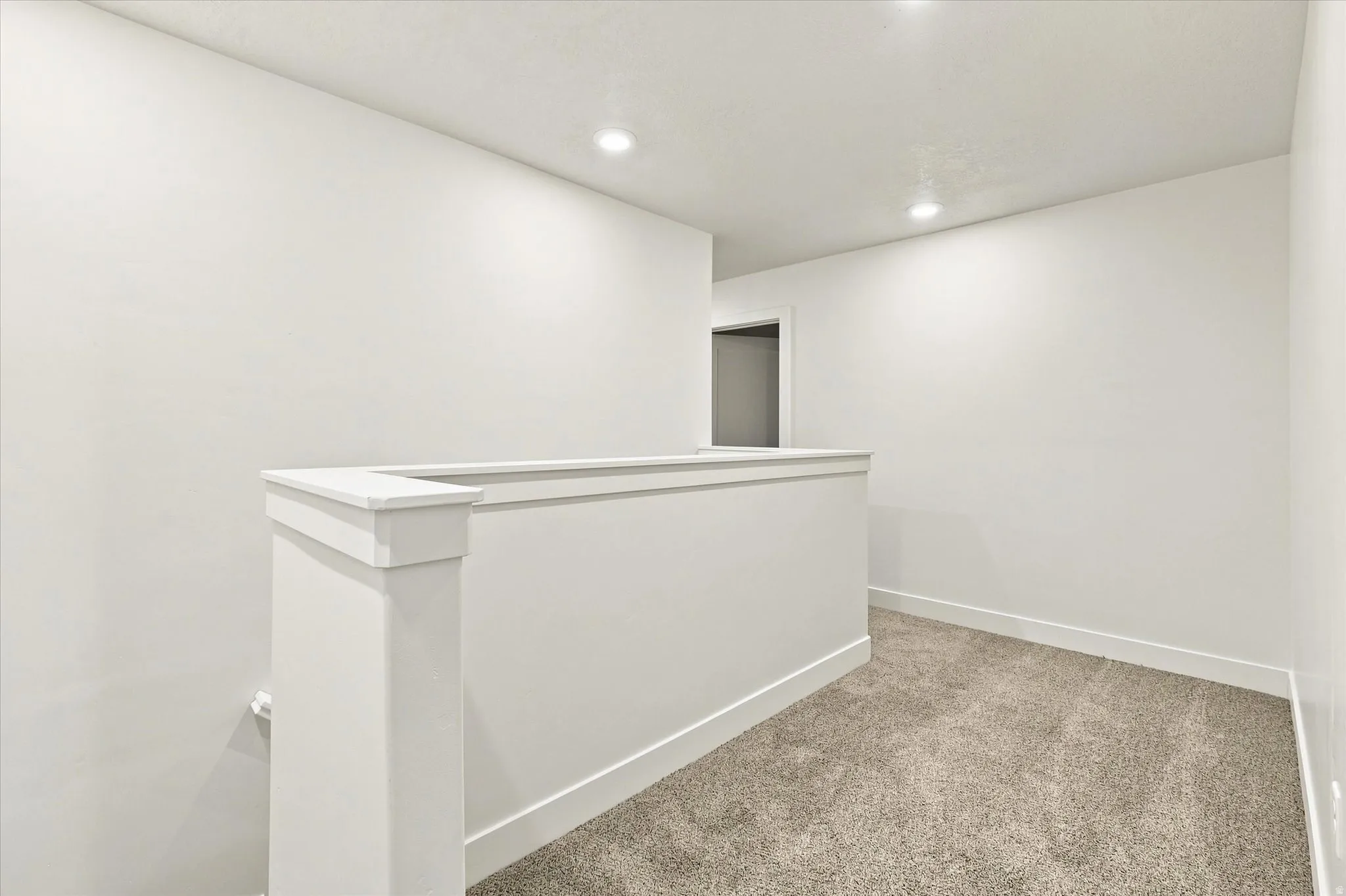Carpeted hallway with white walls, recessed lighting, and white trim