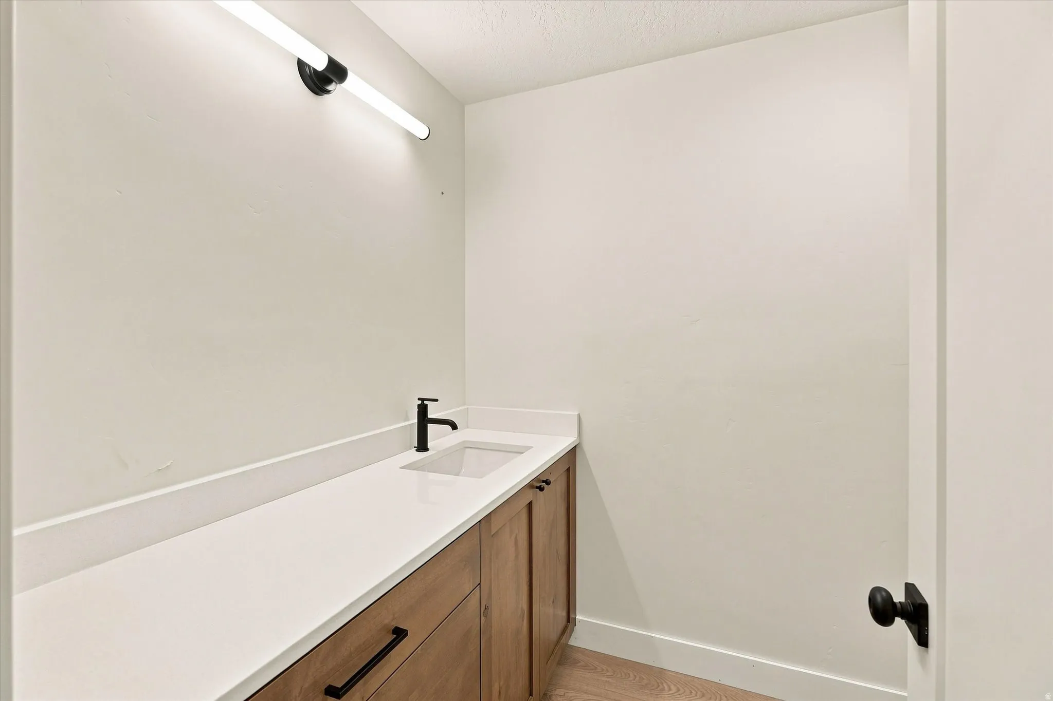 Wood-finish vanity with flat-panel doors, white countertop, integrated rectangular sink, and matte black faucet