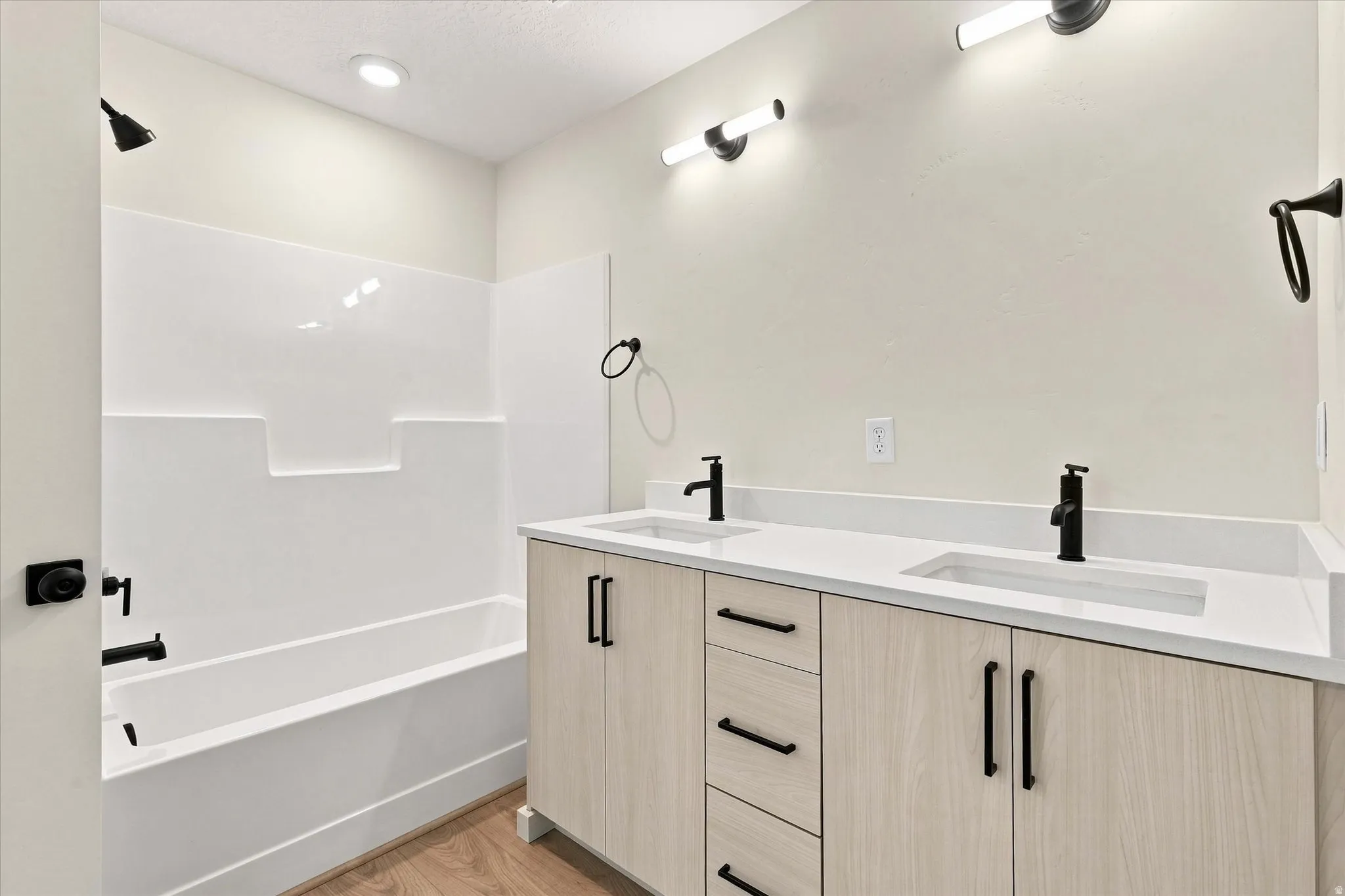 Dual vanity with integrated sinks, light wood-finish cabinetry with matte black hardware, and a white countertop