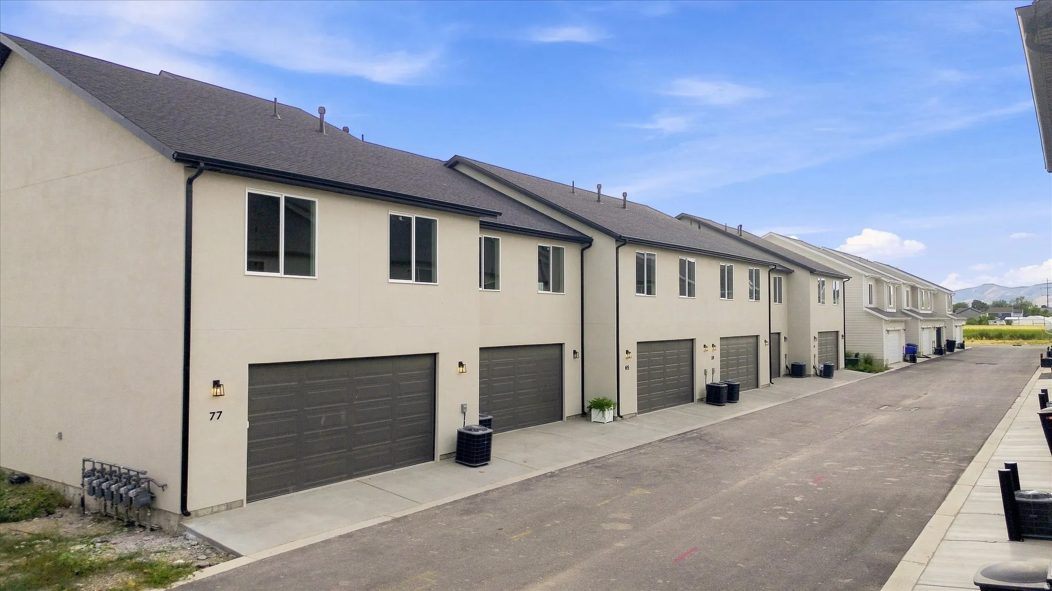 Modern stucco exterior with dark gray garage doors, individual driveways, and black-framed windows