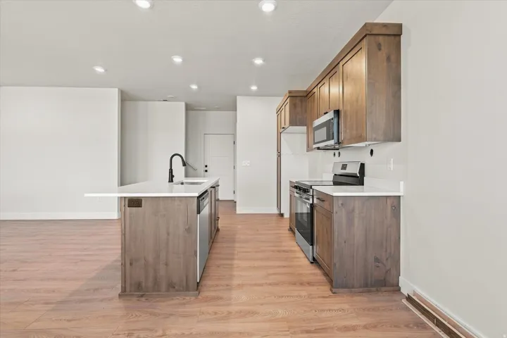 Kitchen featuring wood-finish flooring, recessed lighting, wood cabinetry, a center island with a sink, and stainless steel appliances