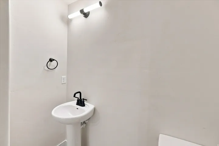 Pedestal sink with a matte black faucet, wall-mounted light fixture, and a black towel ring