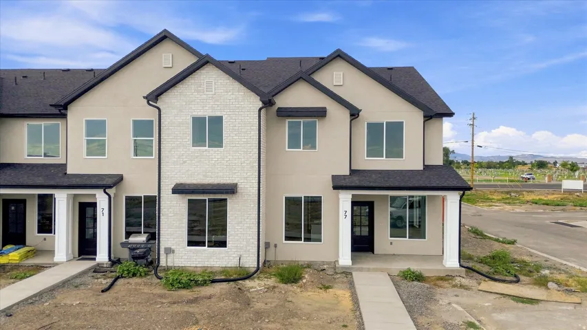 Contemporary townhome featuring a stucco and white brick facade, dark shingle roof, and white-framed windows