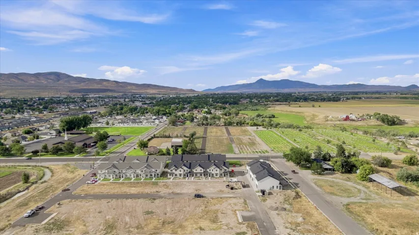 Developing residential area with mountain backdrop, established green spaces, and adjacent agricultural land