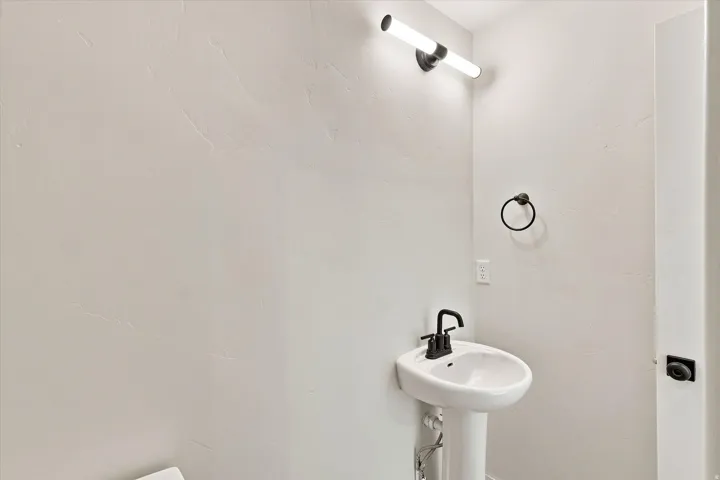 Pedestal sink with a matte black faucet, cylindrical vanity light, and a black circular towel holder
