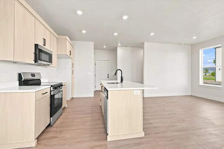 Open-concept kitchen featuring light-toned cabinetry, stainless steel appliances, a center island with a sink, and wood-finish flooring