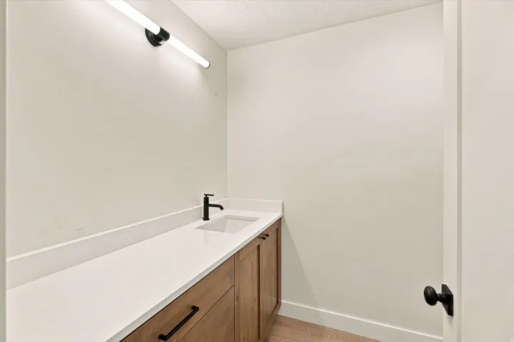 Wood-finish vanity with flat-panel doors, white countertop, integrated rectangular sink, and matte black faucet