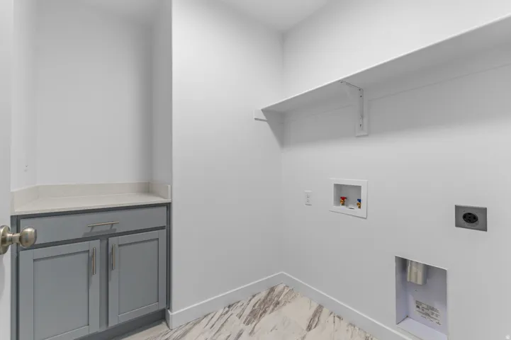 Laundry area featuring a built-in shelf, grey shaker-style cabinetry, light-toned countertop, and wood-finish flooring