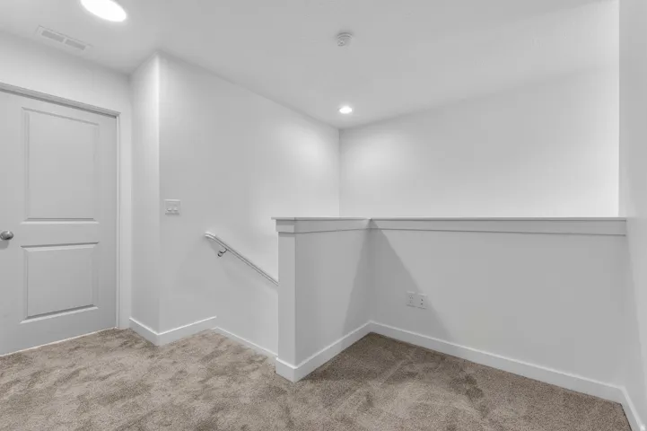 Plush carpet flooring, recessed ceiling lighting, two-panel interior door, and a white handrail