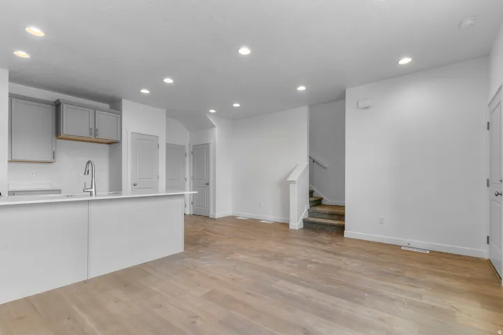 Open-concept living area with wood-finish flooring, recessed lighting, and a modern kitchen island with an integrated sink