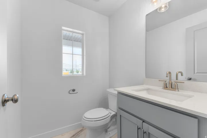 White walls with a window, a toilet, a vanity with a white countertop, a mirror, and a light fixture