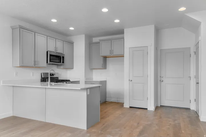 Kitchen featuring light grey cabinetry, stainless steel microwave, gas range, recessed lighting, and light-toned wood-finish flooring