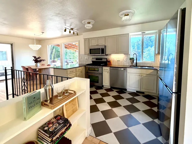 Kitchen featuring checkerboard flooring, stainless steel appliances, light-toned cabinetry, and a dark countertop