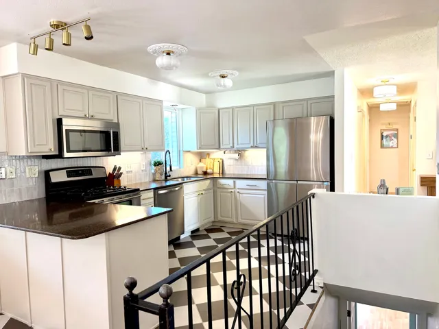 Kitchen with light-toned cabinetry, dark countertops, stainless steel appliances, and a checkerboard floor pattern