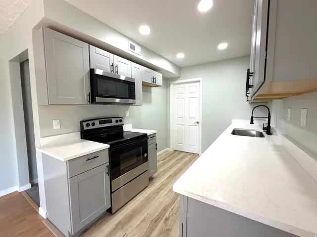 Modern kitchen featuring light gray cabinetry, stainless steel appliances, light-toned countertops, and wood-finish flooring