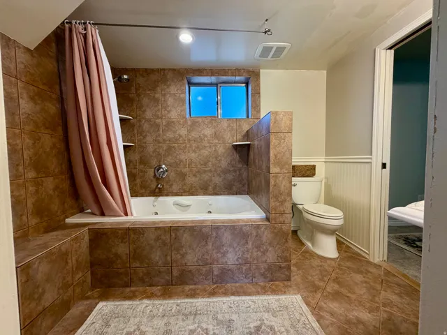 Tiled shower and soaking tub combination with built-in shelving, a window, and a wall-mounted showerhead