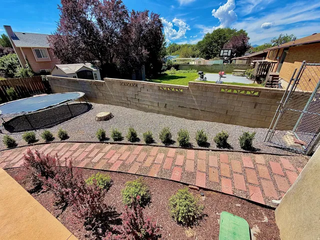 Tiered backyard featuring a brick paver pathway, gravel landscaping, and a concrete block retaining wall