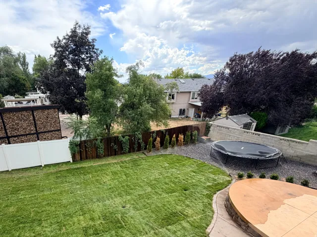 Expansive yard featuring a manicured lawn, a custom hardscape patio, a wood privacy fence, and mature trees