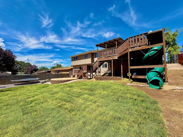 Expansive backyard featuring a manicured lawn, multi-level wooden deck, and a built-in play structure with slides