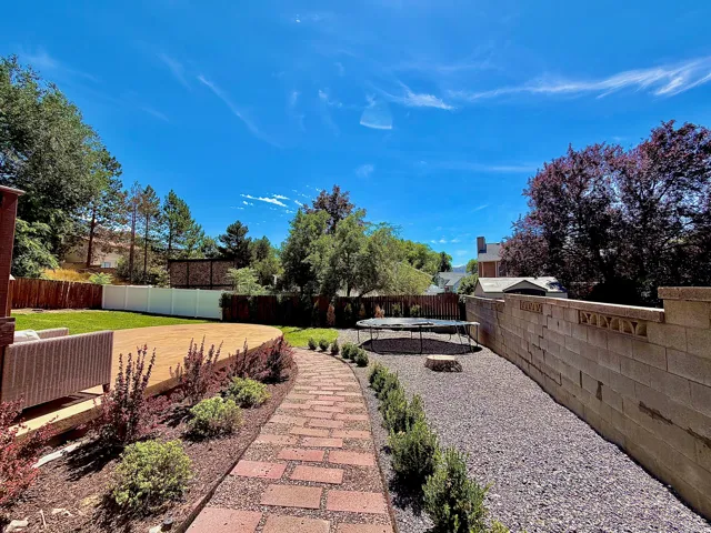 Expansive backyard featuring a curved paver pathway, a large wood-finish deck, a gravel area, and a block retaining wall