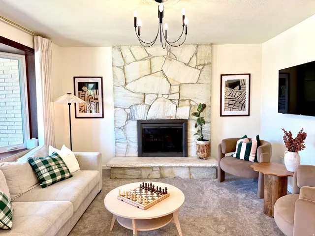 Stone veneer fireplace with a hearth, dark metal firebox, and a black chandelier