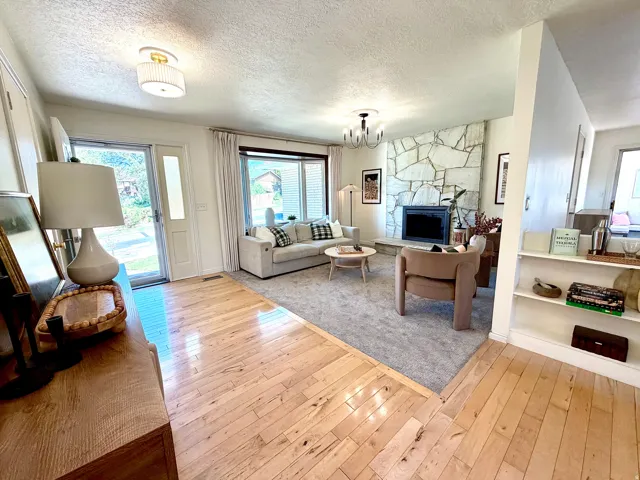 Stone-faced fireplace with a dark-finish firebox, light wood-finish flooring, built-in shelving, and a glass-paneled entry door