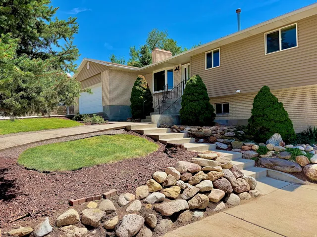 Split-level residence featuring a brick and siding exterior, concrete driveway, attached garage, and a landscaped front yard with stone accents