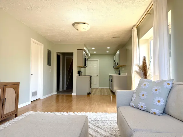 Hardwood-style flooring throughout, light green wall paint, and recessed ceiling lighting in the kitchen area