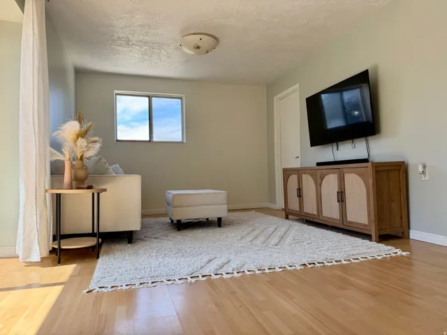 Hardwood flooring, light-colored walls, ceiling-mounted light fixture, window with natural light, and a white door with dark hardware