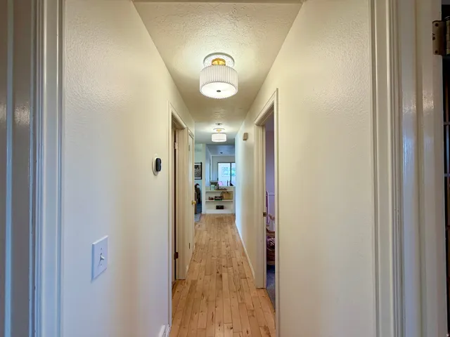 Hallway featuring warm wood-finish flooring, white painted walls, and recessed ceiling lighting throughout