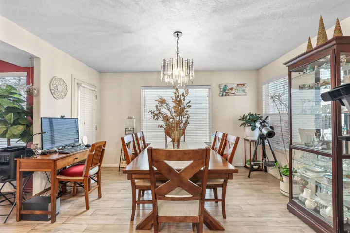 Recessed ceiling with a chandelier, wood-finish flooring, and multiple windows with horizontal blinds