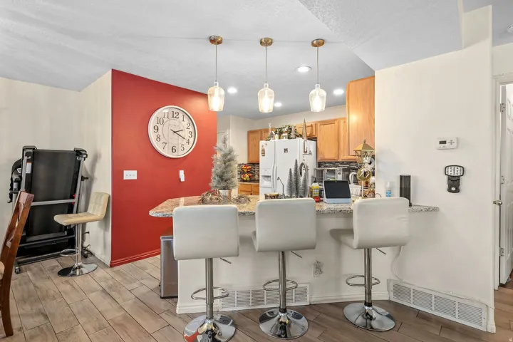 Kitchen peninsula with a stone-finish countertop, pendant lighting, and wood-finish flooring