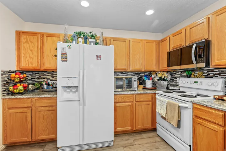 Wood-finish cabinetry, tile flooring, granite-style countertops, and a mosaic tile backsplash