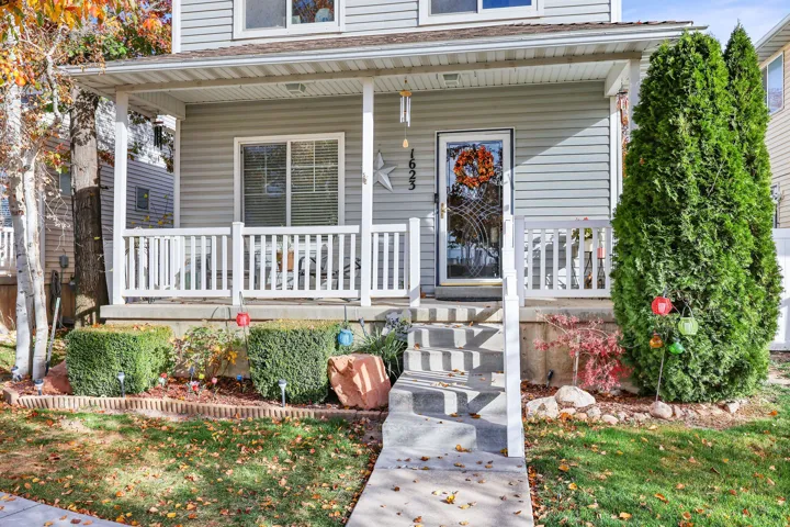 Exterior featuring siding, a covered porch with white railings, a concrete walkway, and established landscaping