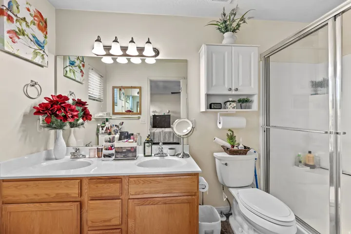 Dual vanity with white countertops, wood-finish cabinetry, a large wall-mounted mirror, and a glass-enclosed shower