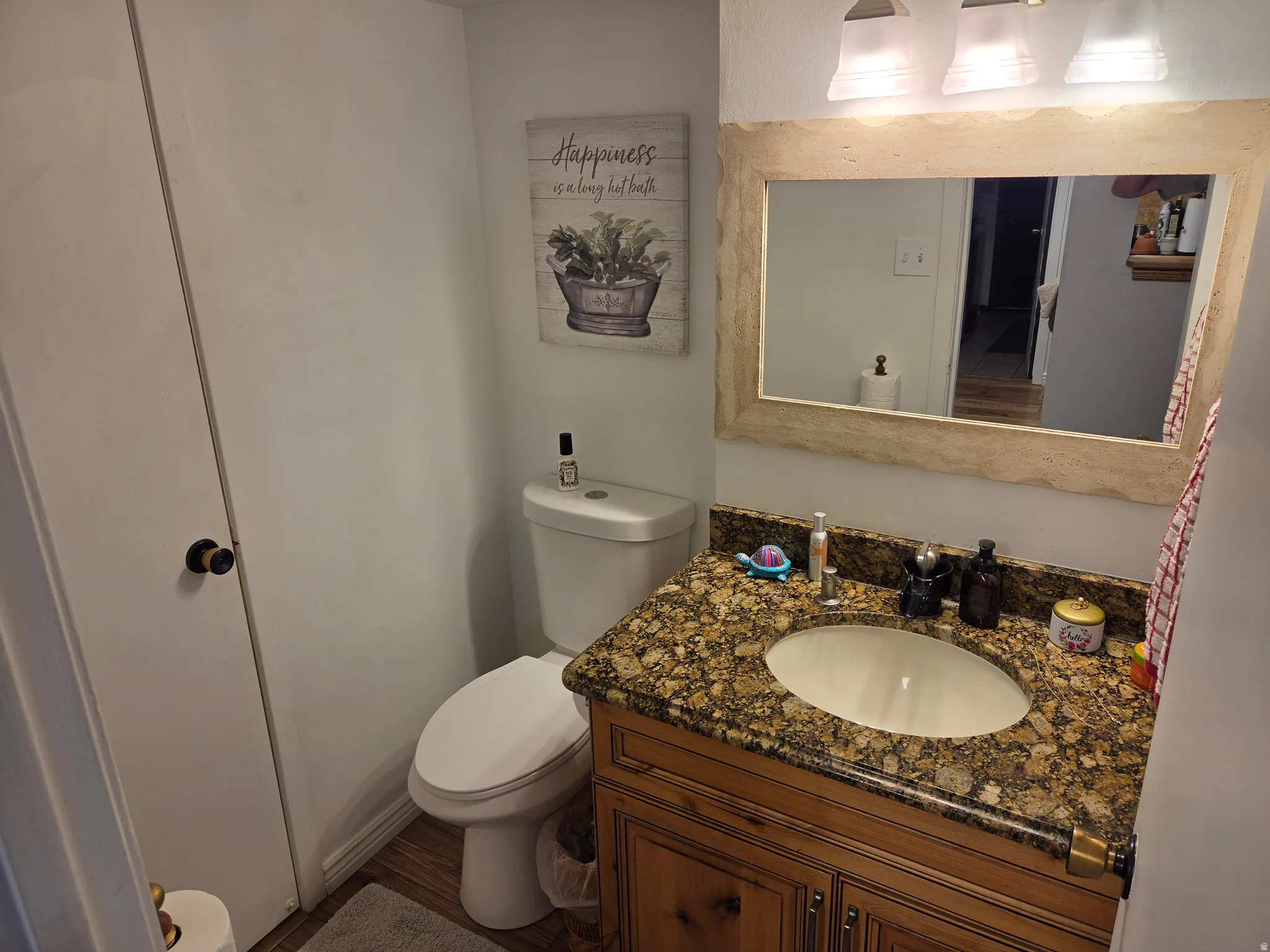 Vanity with stone countertop, undermount sink, wood-finish cabinetry, and framed mirror with integrated lighting