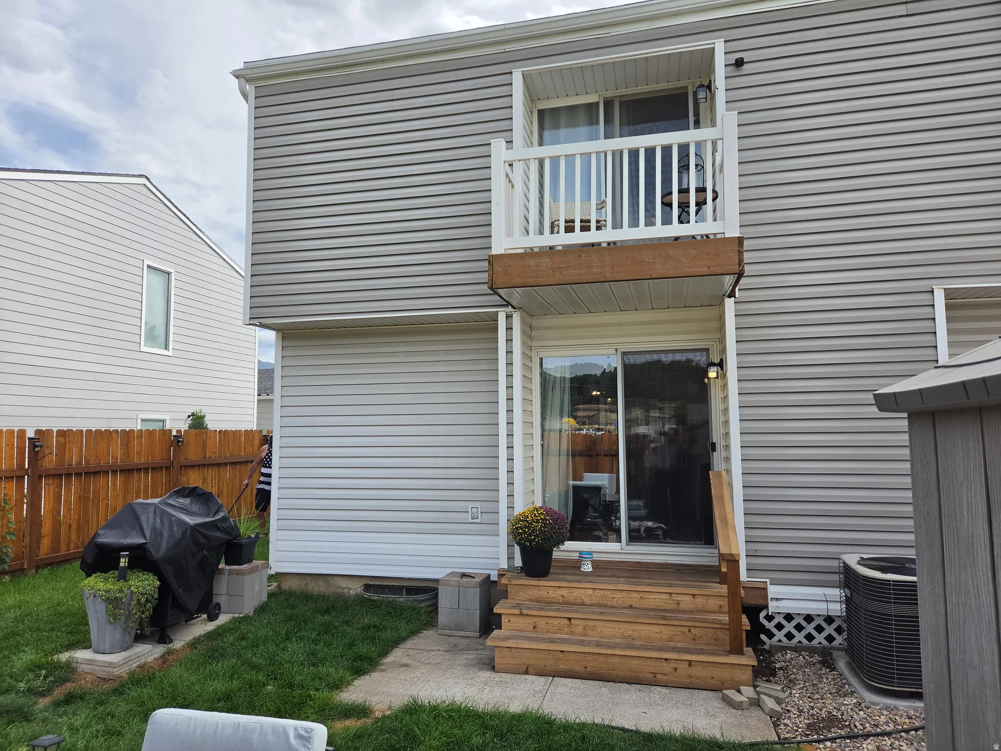 Two-story exterior with horizontal siding, a second-story balcony with white railing, and a ground-level wood deck leading to sliding glass doors