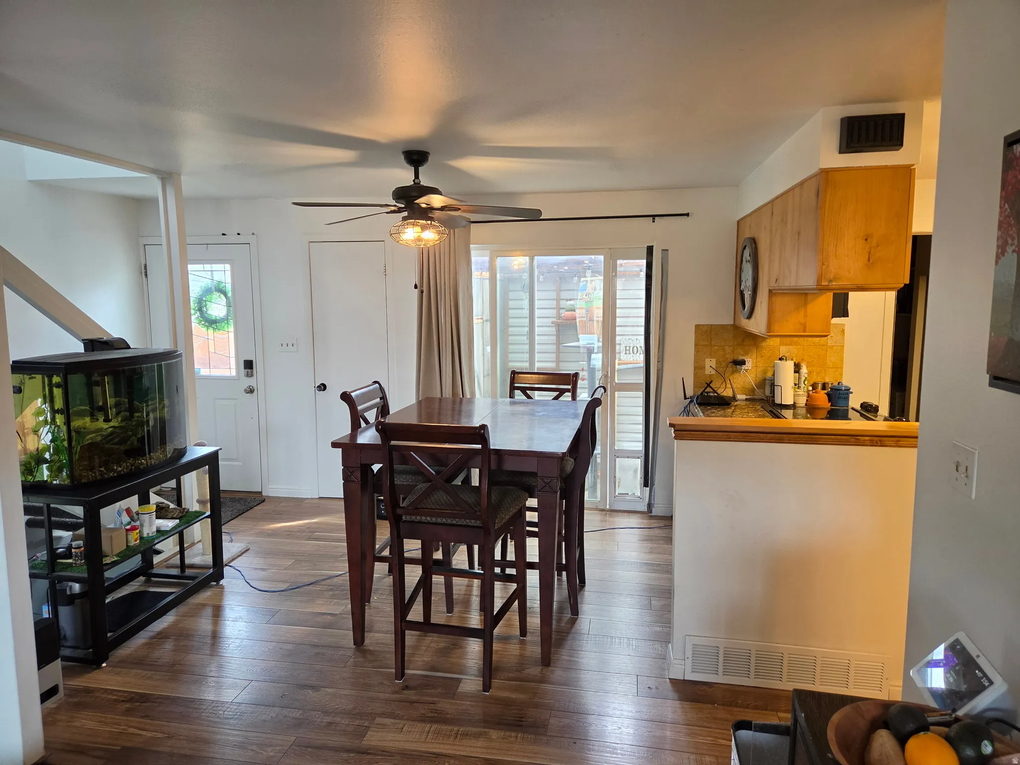 Wood-finish flooring, ceiling fan with integrated lighting, wood cabinetry, and a kitchen counter with backsplash