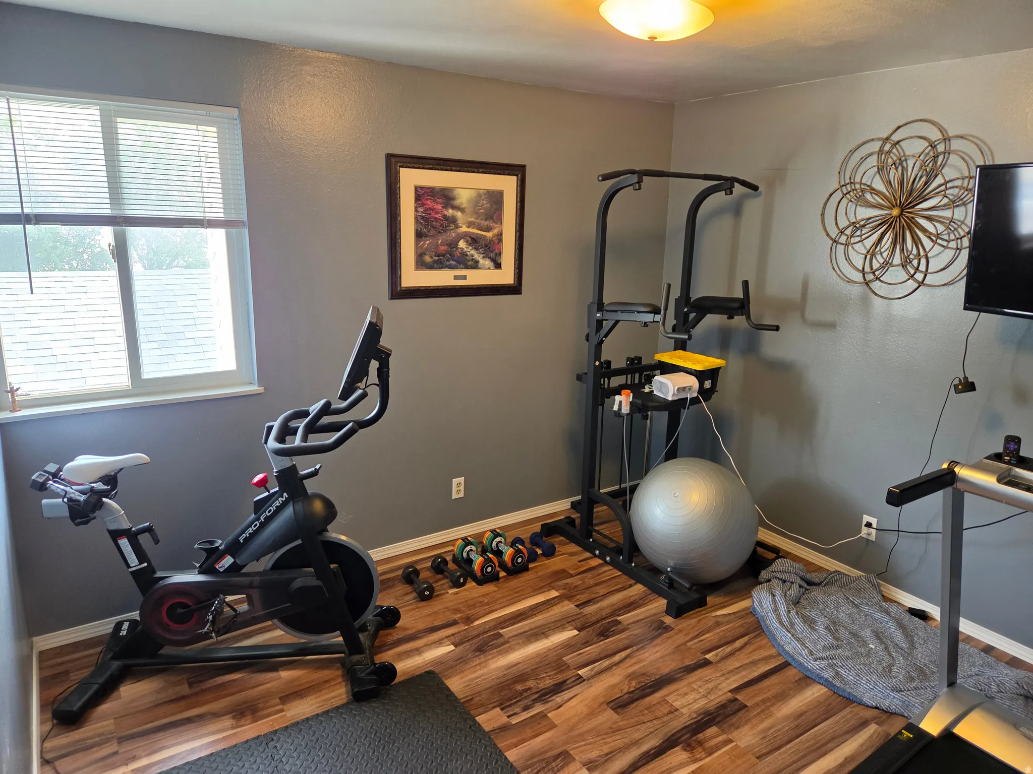 Wood-finish flooring with a neutral wall color, overhead lighting, and a window with blinds