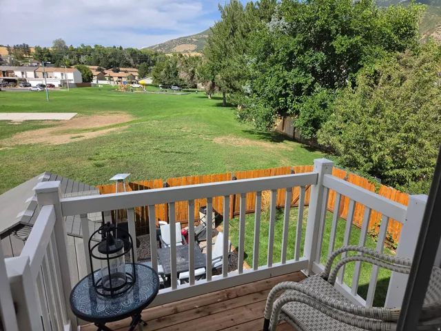 Outdoor deck with white railing overlooking a fenced yard and expansive green space