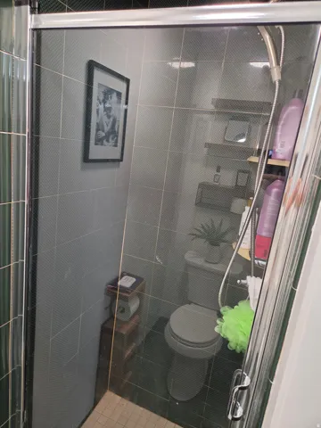 Glass-enclosed shower with a handheld shower fixture, dark tile flooring, and integrated wall shelving