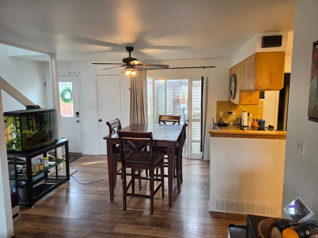 Wood-finish flooring, ceiling fan with integrated lighting, wood cabinetry, and a kitchen counter with backsplash