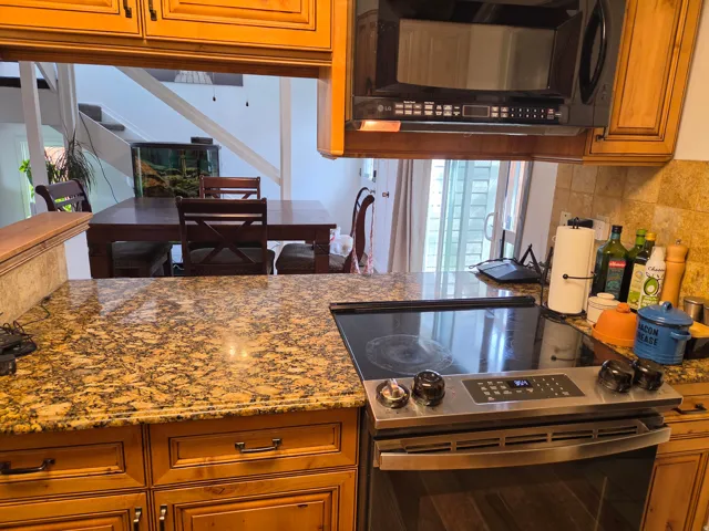 Kitchen featuring granite countertops, wood cabinetry with dark hardware, a built-in microwave, and a stainless steel electric range