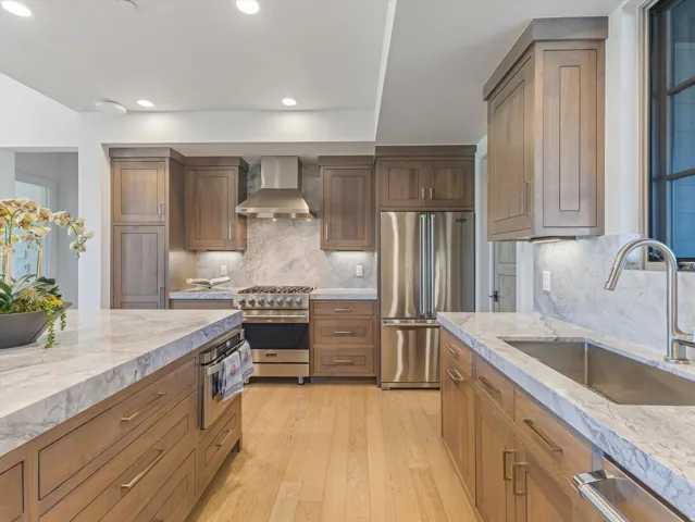 Kitchen featuring wood cabinetry, light-toned wood-finish flooring, stainless steel appliances, marble countertops, and a stone backsplash