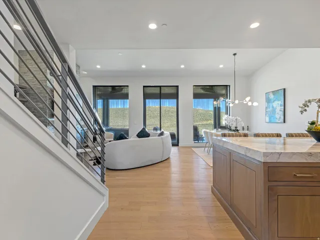 Open-concept living area with wood-finish flooring, a contemporary staircase with metal balusters, and a kitchen island featuring a light-toned countertop