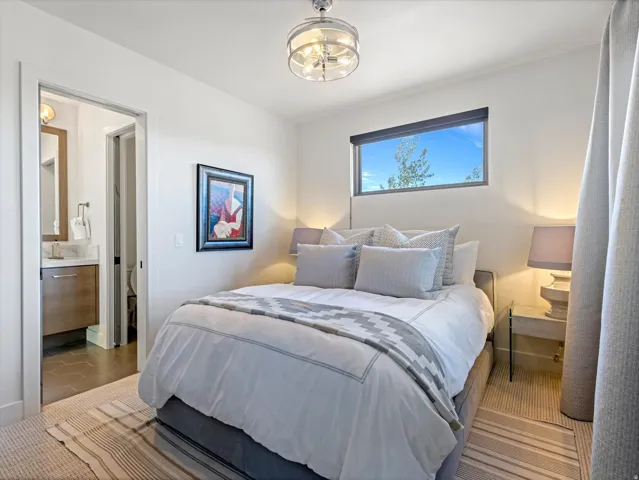 Recessed window with exterior scenery, overhead drum pendant light, carpeted flooring, and an en-suite bathroom featuring a vanity with a rectangular basin sink and a stone countertop