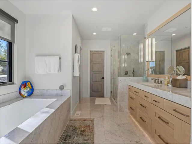 Spacious bathroom featuring a built-in soaking tub, dual vanity with undermount sinks, wood-finish cabinetry, and a glass-enclosed shower