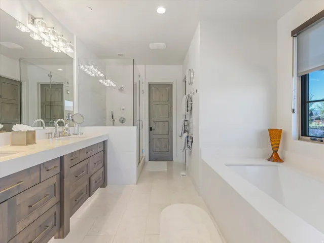 Dual vanity with undermount sinks, frameless glass shower, built-in soaking tub, and tile flooring