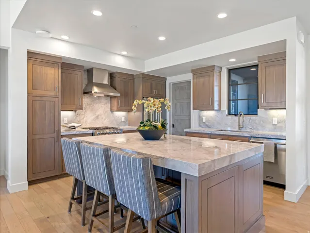 Kitchen featuring wood cabinetry, a large center island with a stone countertop, stone backsplash, stainless steel appliances, and recessed lighting