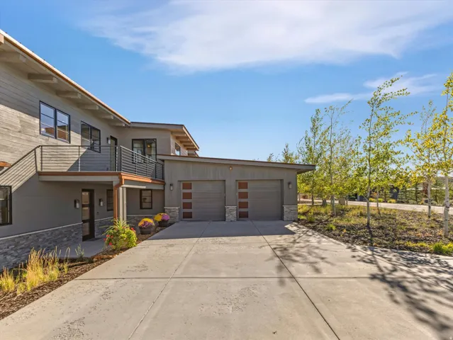 Sloped roofline, contemporary exterior siding, stone accents, two-car garage with modern doors, and a concrete driveway